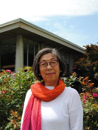 Photo of Kayo in front of the Mabel Smith Douglass library, wearing a white long sleeve top and a pink and orange scarf