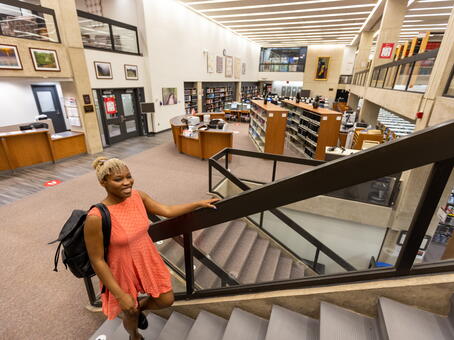 A student walking up the stairs in the Smith library. The main area of the library is in view in the background