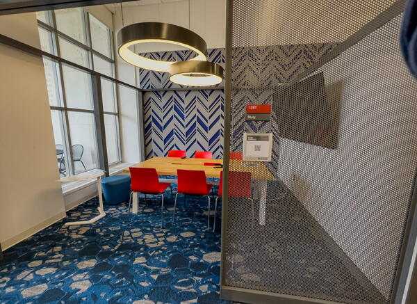 Interior of group study room with a large table, chairs, a wall-mounted display, and circular, hanging lights