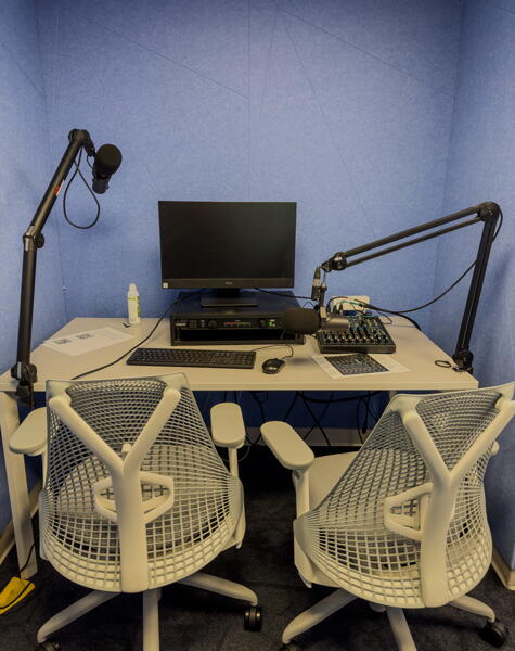 Two chairs at an audio podcast station with a computer and microphones