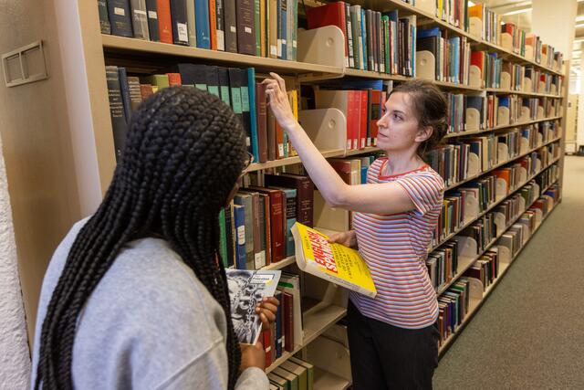 Photo of a Dana staff member pulling a book from the shelf to assist a student with their needs