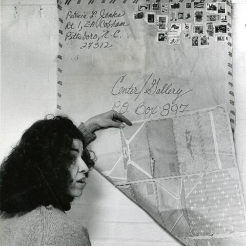 Black and white photo of a woman looking at an artwork designed like a postcard