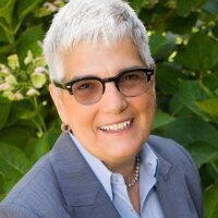 Headshot of Myers, smiling with short white hair wearing a blue dress shirt and a blazer