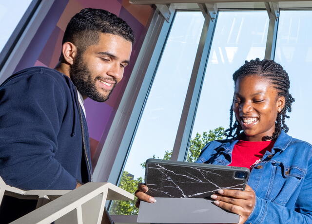 Two smiling students looking at tablet