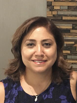 Photo of Mina, she is smiling and wearing a blue tank top with a brick design background