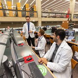 Students working on computers in the main area of the Smith library talking with another student