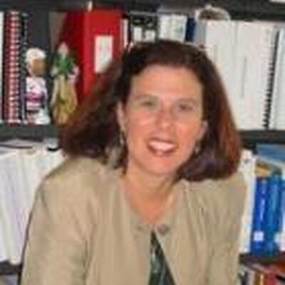 Photo of Judy, wearing a beige sweater and depicted in front of book shelves