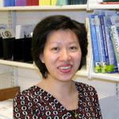 Image of Mei, wearing a dark patterned shirt in front of book shelves