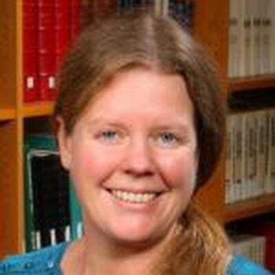 Photo of Megan, she is wearing a blue shirt and in the background is book shelves