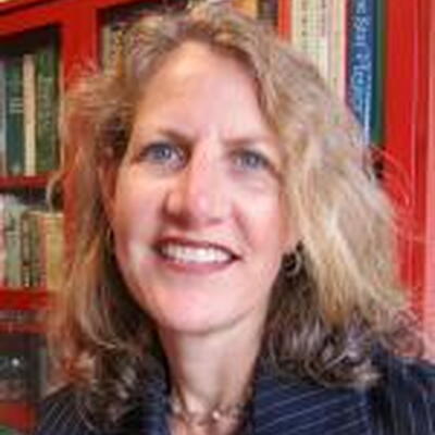 Photo of Victoria, wearing a blue collared shirt in front of books on book shelves.