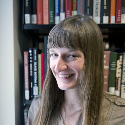 Headshot of Elizabeth smiling and standing in front of a book shelf filled with colorful books