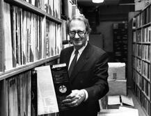 Black and white photo of Dan Morgenstern, former director of the Institute of Jazz Studies, pulling out a record from the IJS collection